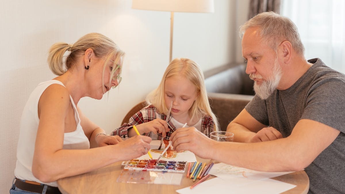 A family of three enjoying creative time with painting and drawing at home.